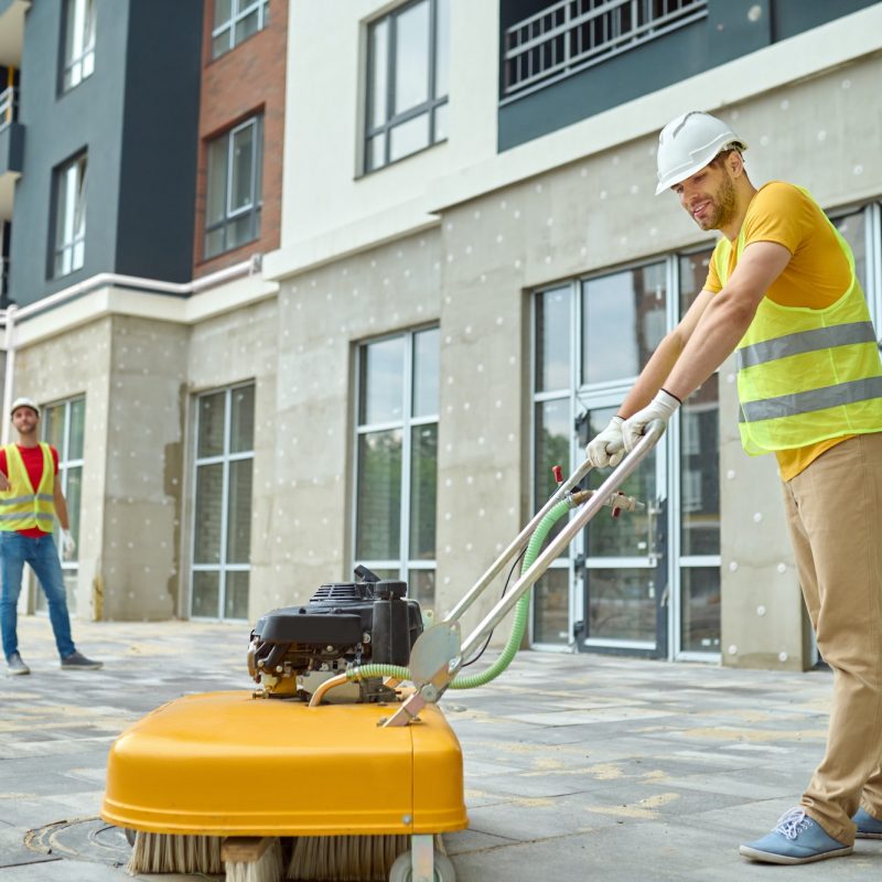 worker-cleaning-construction-site-and-two-men-near-building.jpg